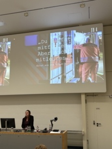 Anne Blume hält den Vortrag. Hinter ihr ist ein Bild zu sehen mit einem Rettungssanitäter und dem übergeblendeten Text „Du darfst mitfühlen. Aber nicht mitleiden.“